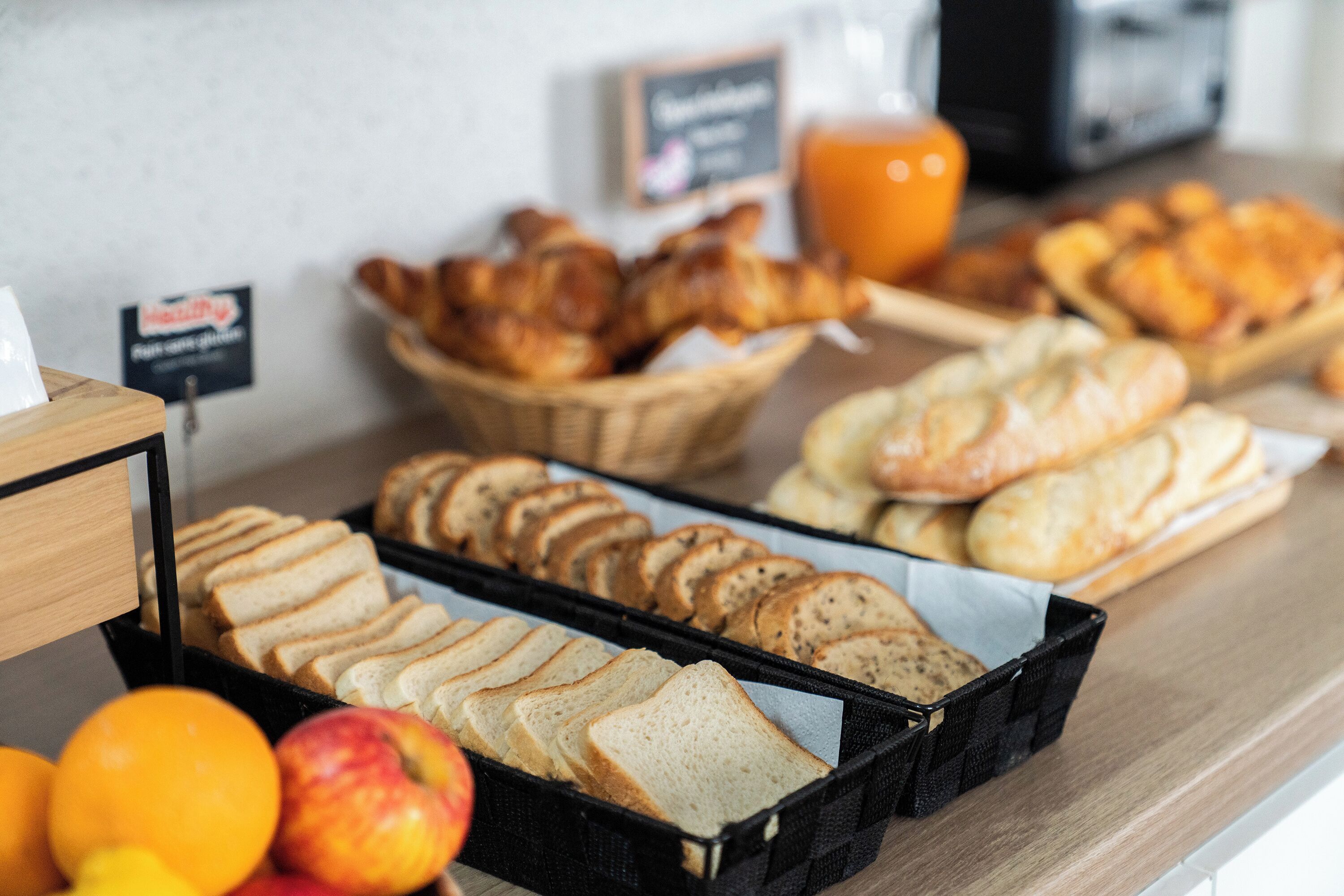 A breakfast buffet with various bread options, pastries, and fresh fruits.