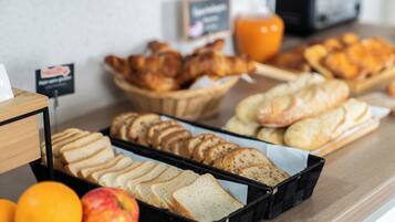 A breakfast buffet with various bread options, pastries, and fresh fruits.