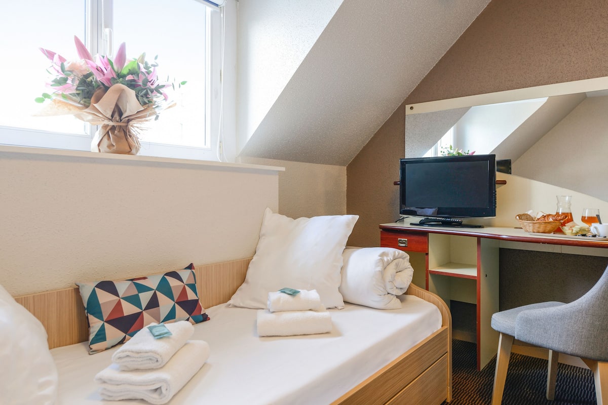 Habitación de hotel con cama, escritorio con computadora, silla y ventana con vistas.