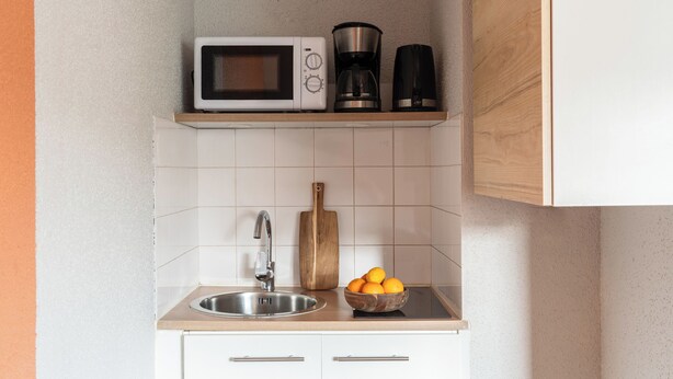 Une cuisine équipée d’un four à micro-ondes, d’une machine à café et d’un saladier rempli d’oranges posé sur le comptoir.