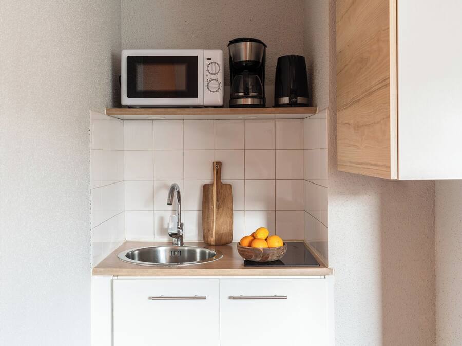 A kitchen with a microwave, coffee maker, and a bowl of oranges on the counter.
