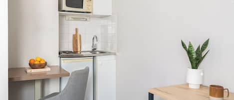 Cocina compacta con microondas, lavamanos y un pequeño comedor con una silla y una mesa.