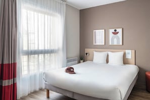 Una habitación de hotel con una cama, una mesita de noche, una lámpara y dos cuadros en la pared.