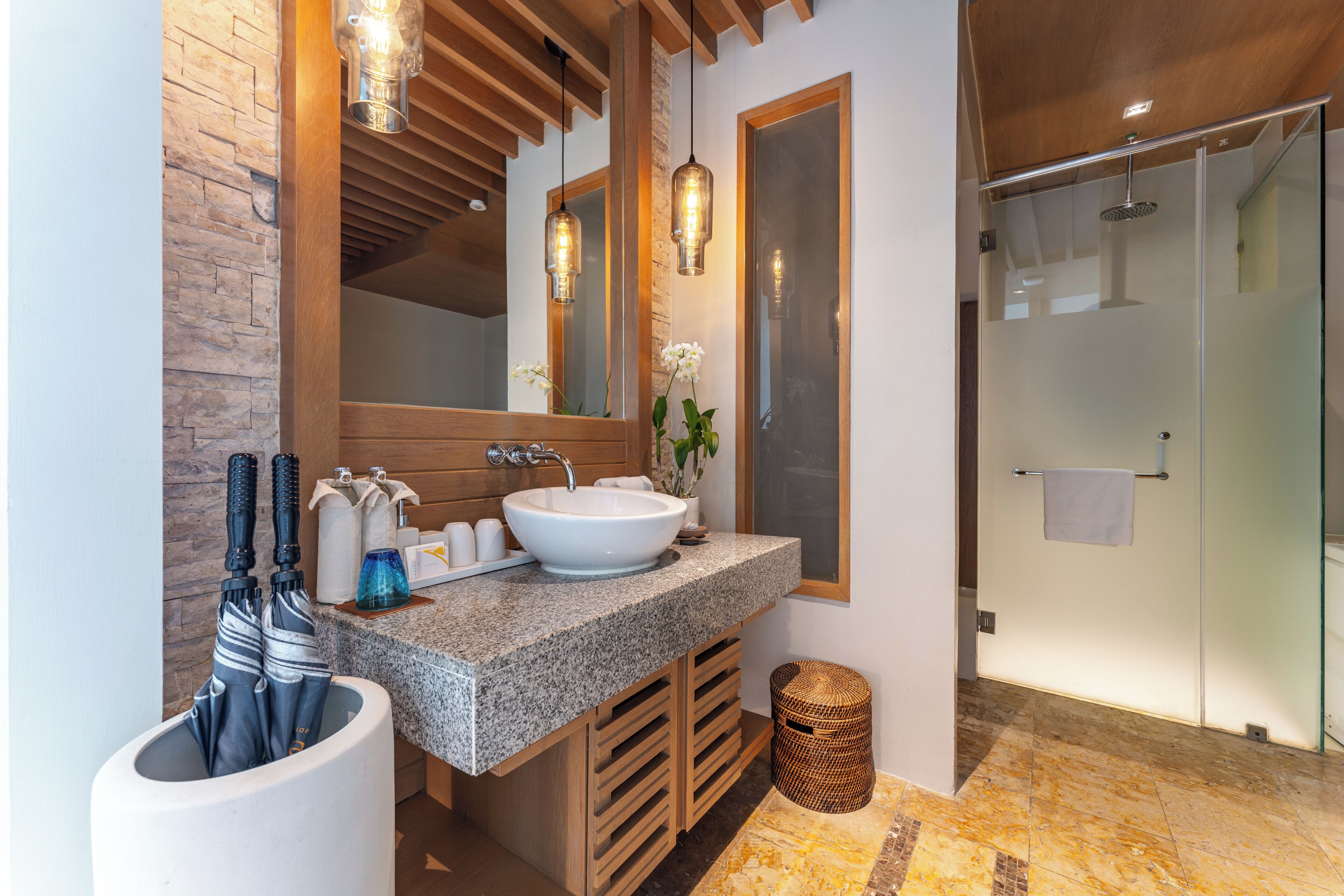 A modern bathroom with a large sink, wooden accents, a glass shower, and a mirror with pendant lights.