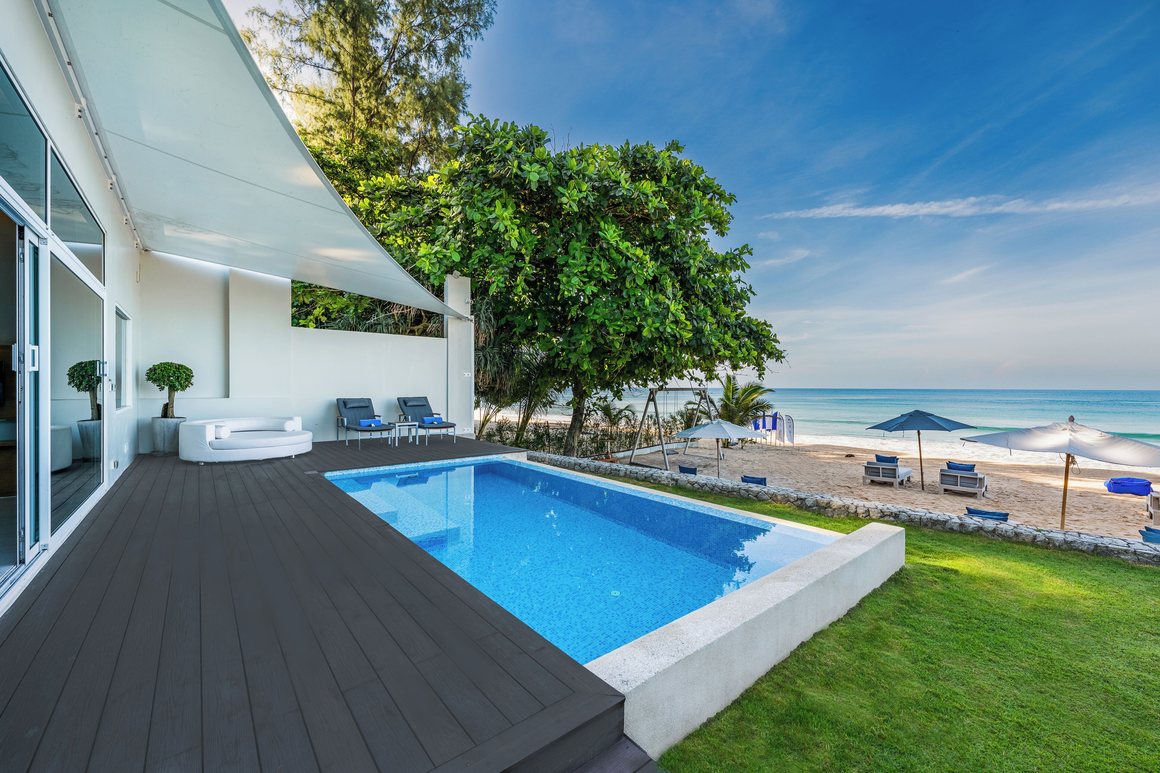 Un área de piscina moderna con vistas despejadas al océano, rodeada por una terraza y sillones de descanso.