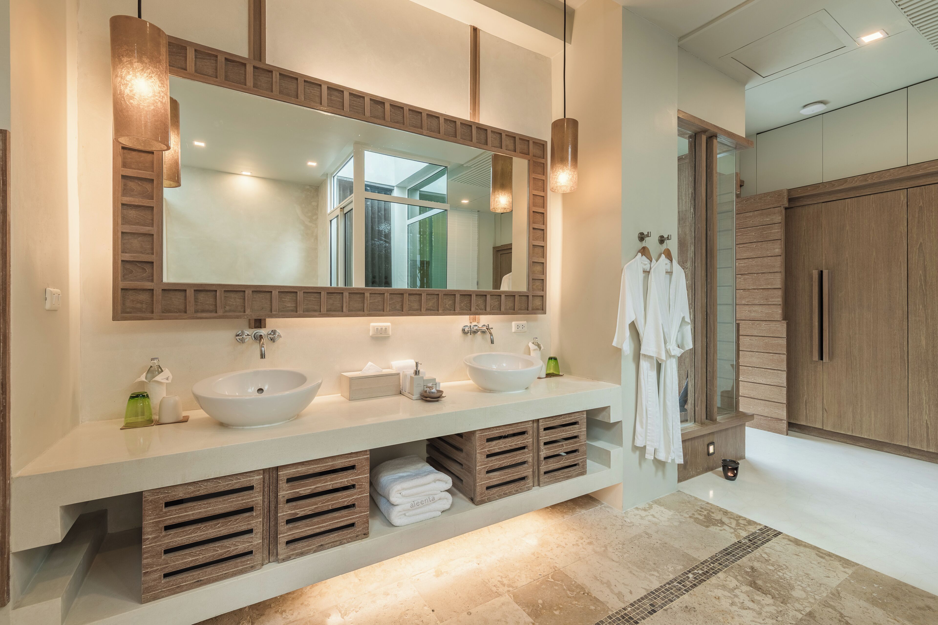 A modern bathroom with a large mirror, two sinks, wooden cabinets, and a tiled floor.