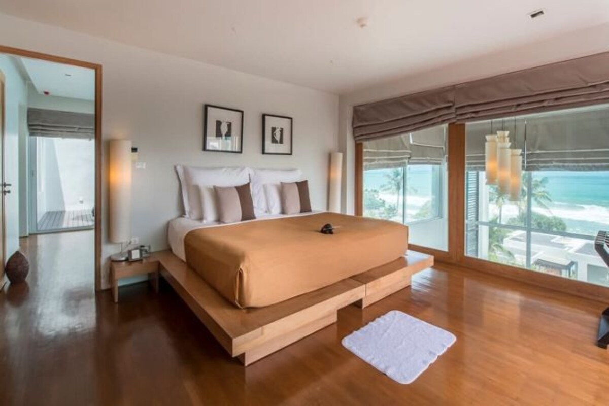A modern bedroom with a large bed, wooden platform, and a view of the ocean.