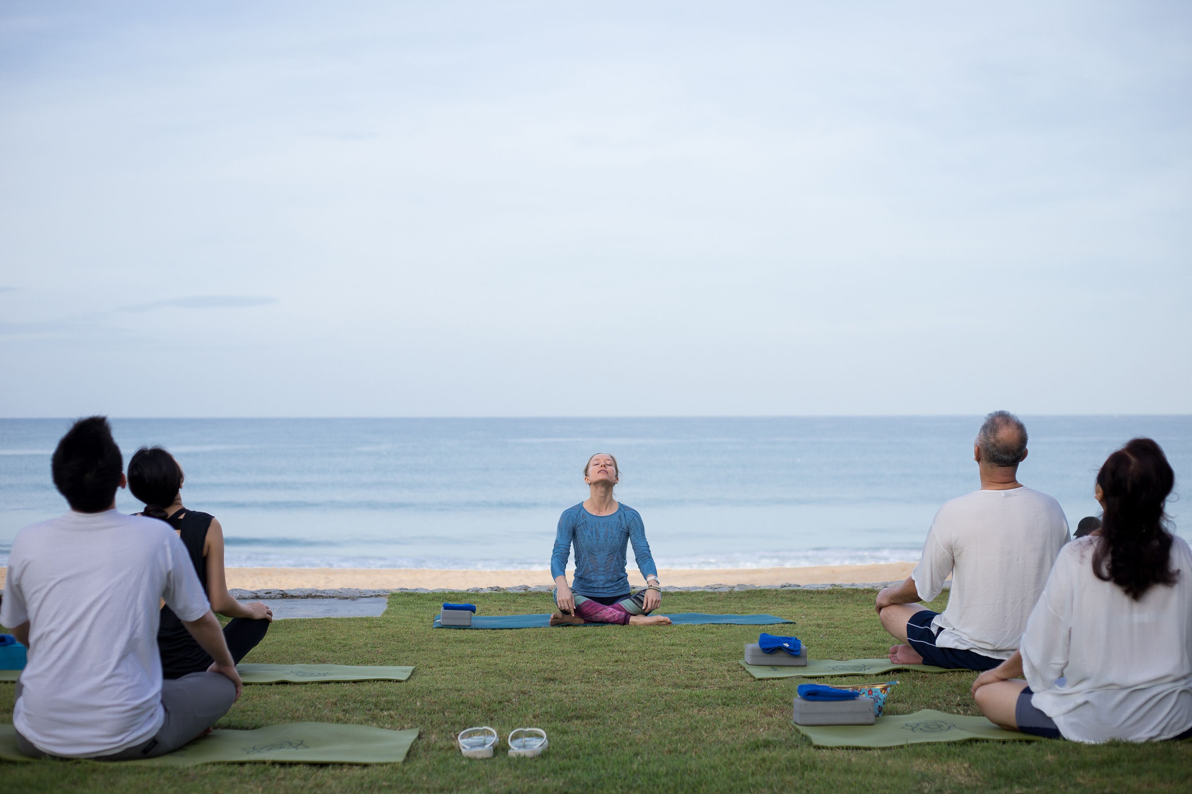 Un grupo de personas sentadas sobre esterillas de yoga en el césped mirando al océano.