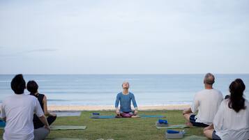 Un grupo de personas sentadas sobre esterillas de yoga en el césped mirando al océano.