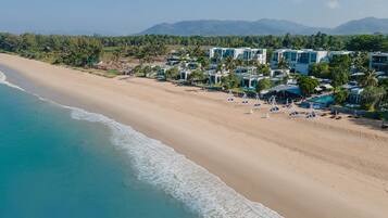 A beach resort with multiple buildings, a sandy beach, and a clear view of the ocean.