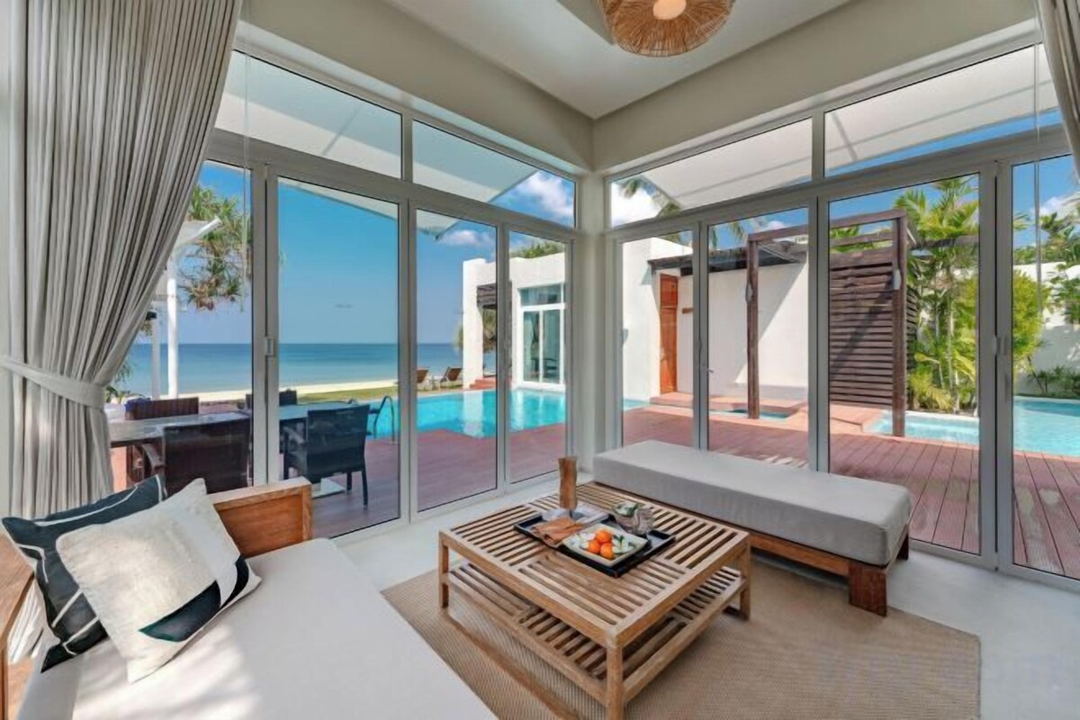 A modern hotel room with a large glass door leading to a pool area, a seating area with a bench, and a wooden coffee table.