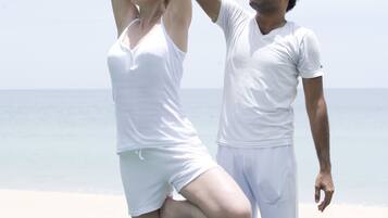 Two people practicing yoga on a mat by the beach.