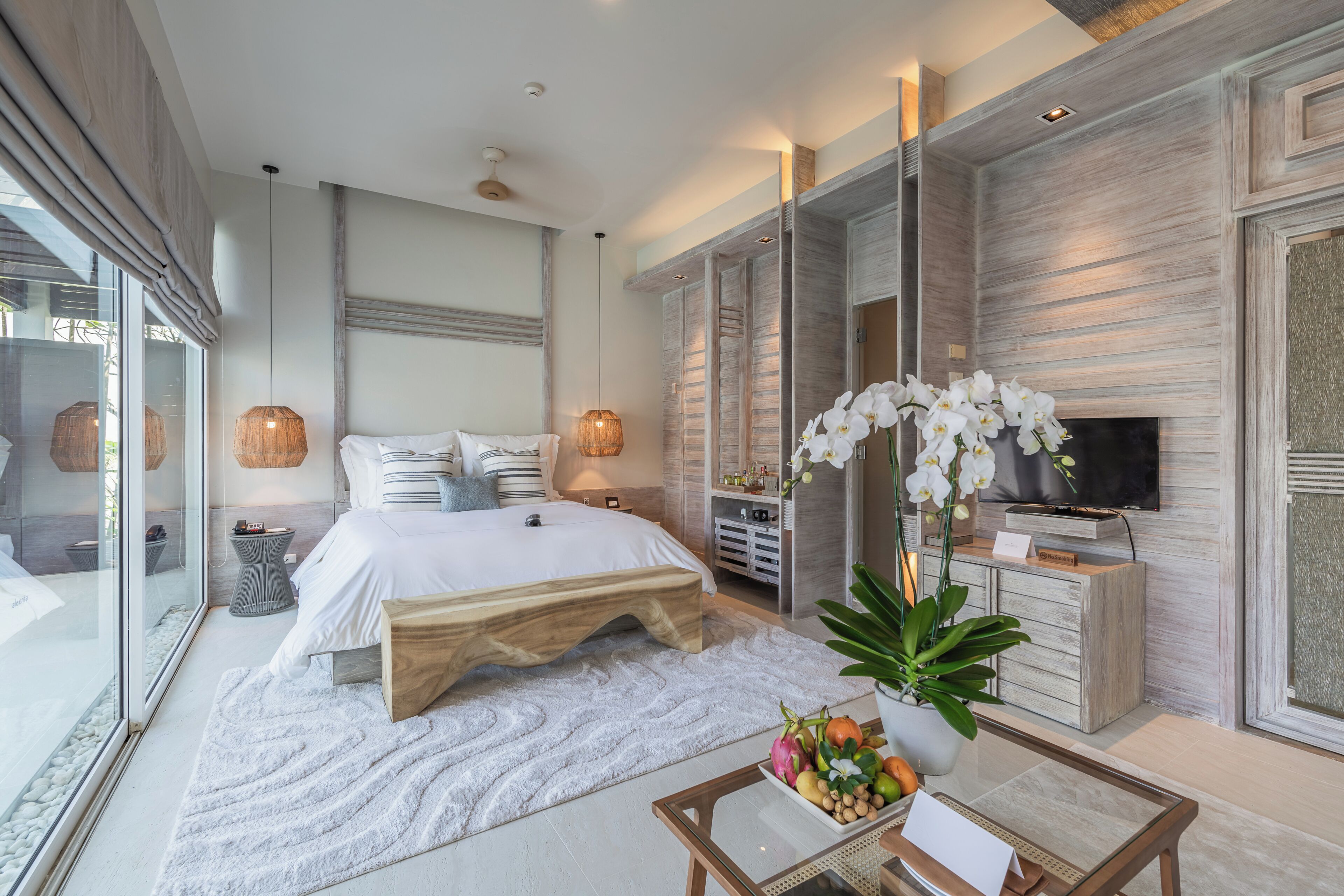 A modern bedroom with a large bed, bedside tables, a TV, and a glass wall.