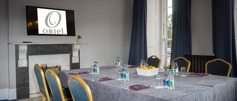 A conference room with a marble table, blue upholstered chairs, a television displaying 'ORIEL', and a fireplace.