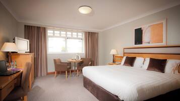 Een hotelkamer met een bed, bureau, stoel en een klein tafeltje met een lamp.