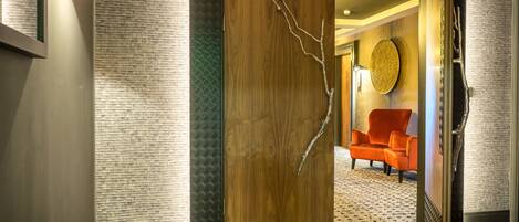 A wooden door with a branch design, leading to a room with a patterned carpet and an orange chair.
