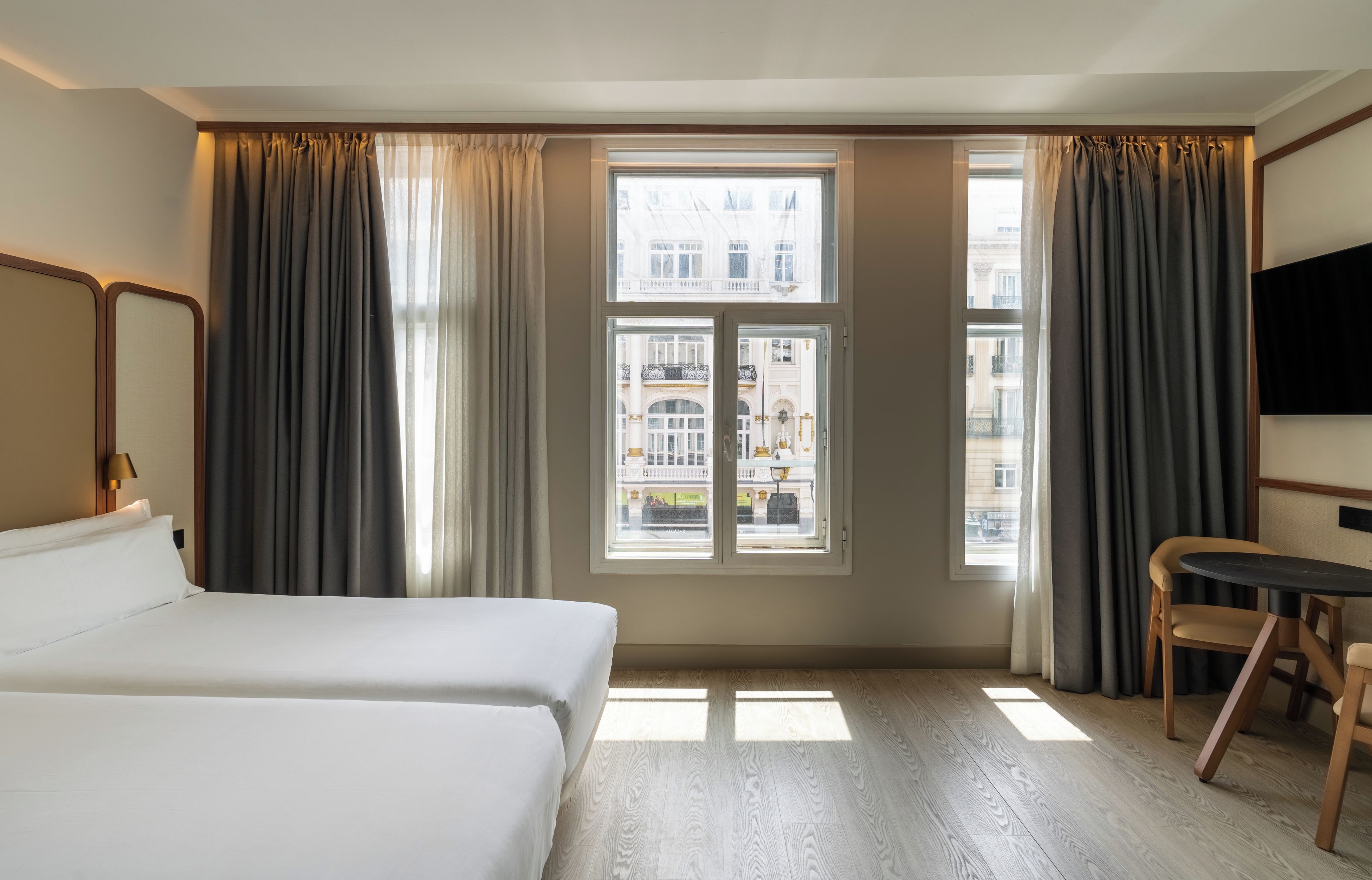 Una habitación de hotel con una cama, un escritorio y vistas a edificios a través de una ventana.