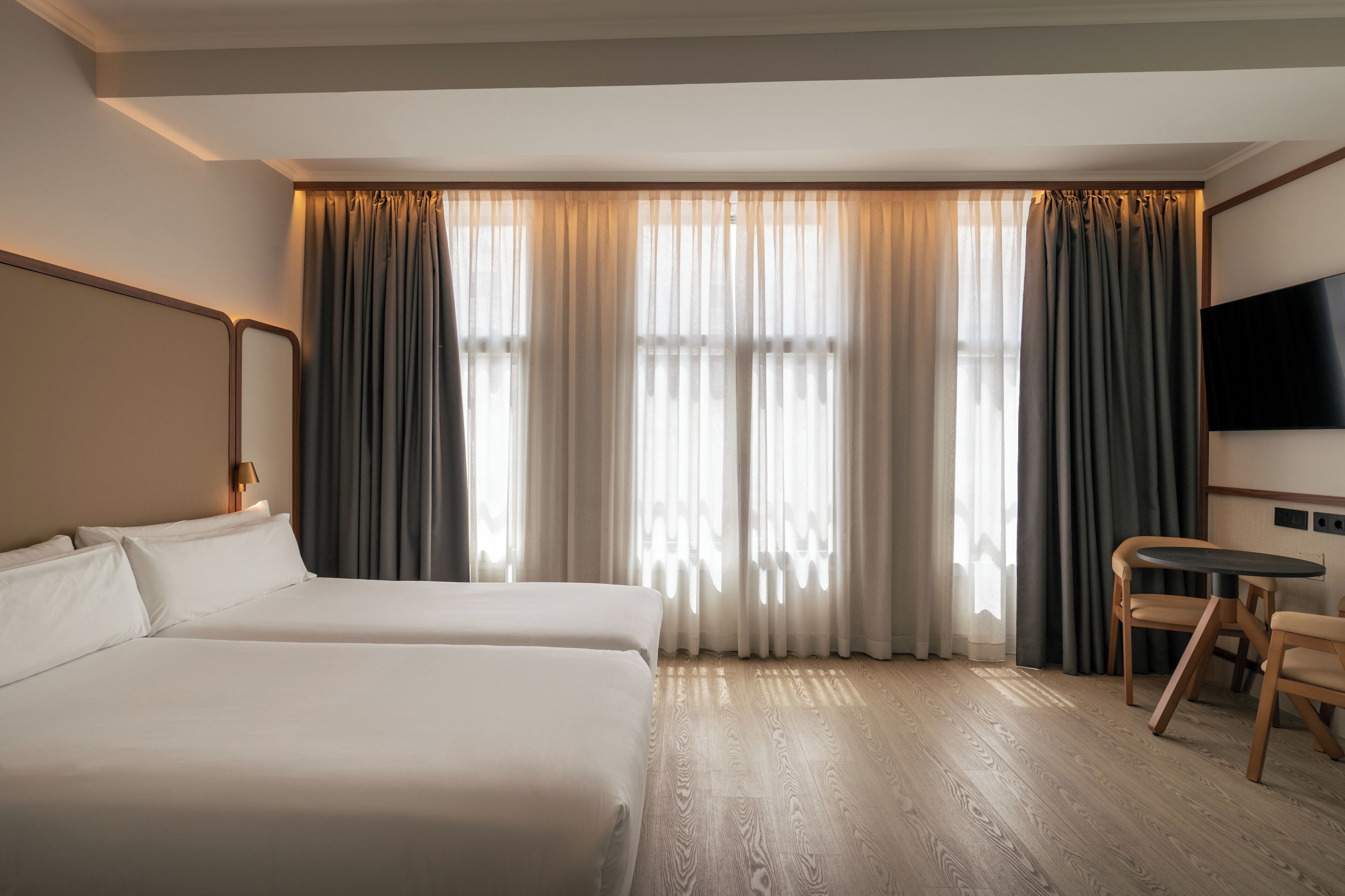 A hotel room with two beds, a television, a small table, and a chair.