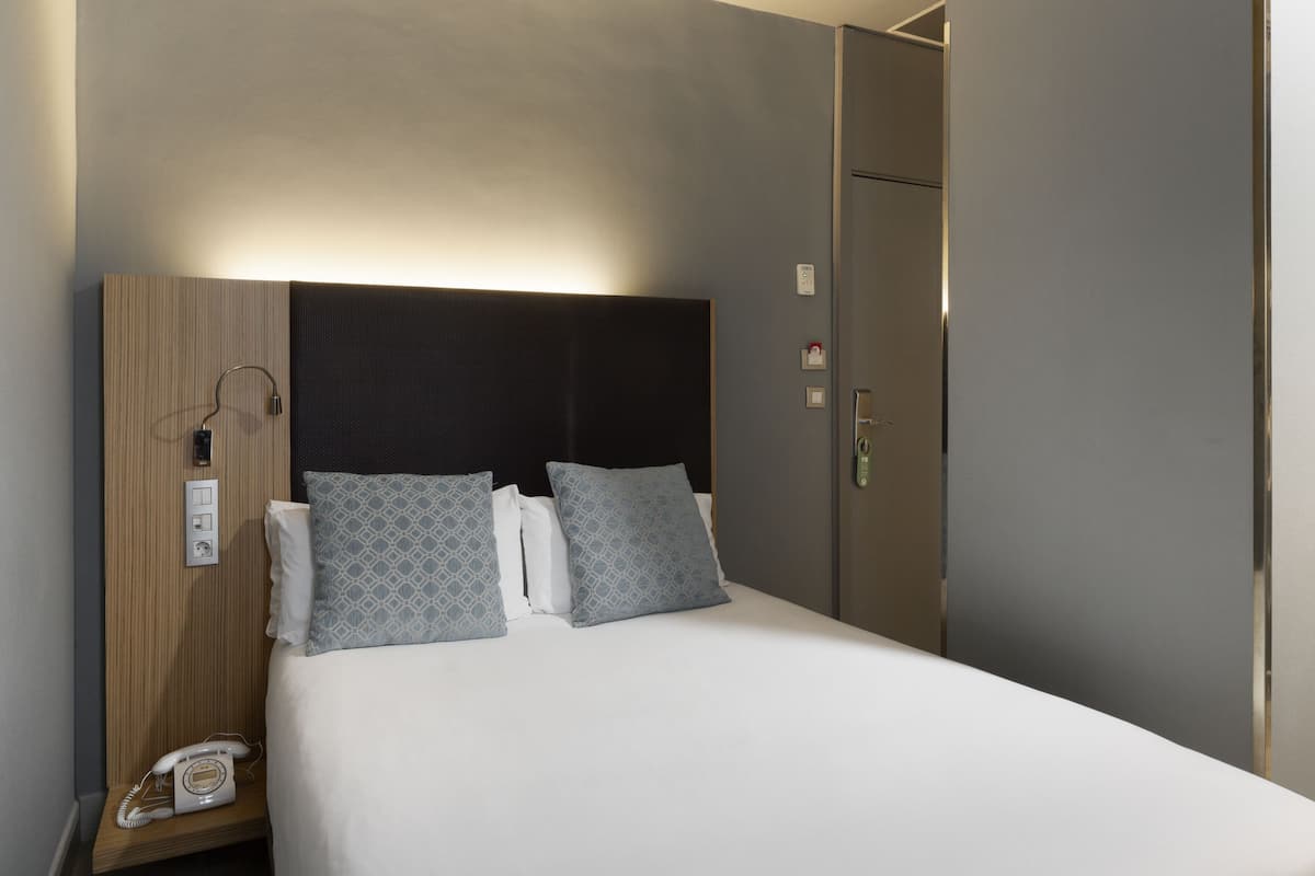 Una habitación de hotel con cama, teléfono junto a ella y armario.