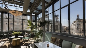 Una habitación luminosa con amplios ventanales, una mesa de mármol y plantas en macetas.