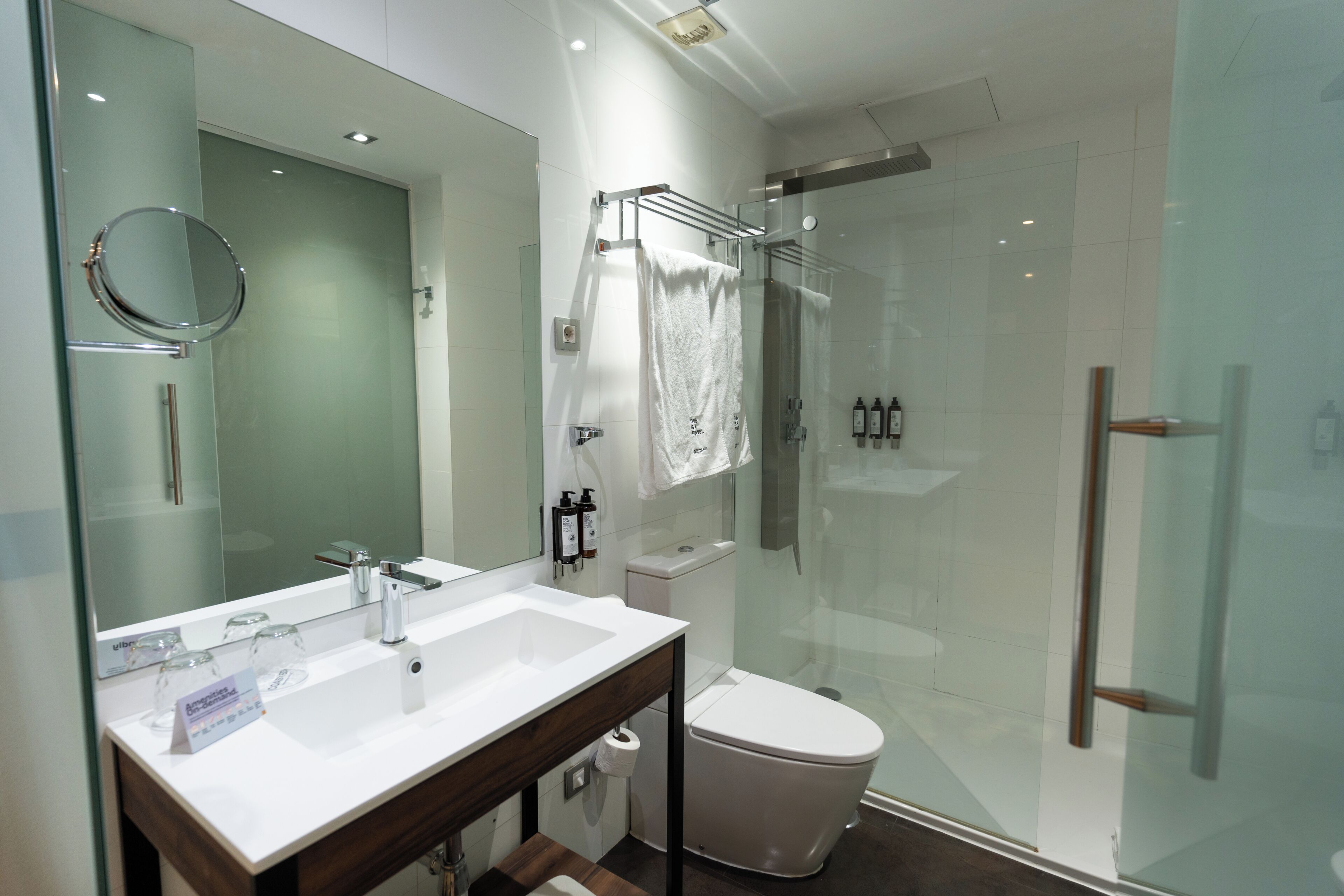 Un bagno moderno con box doccia in vetro, lavandino bianco con specchio e water.