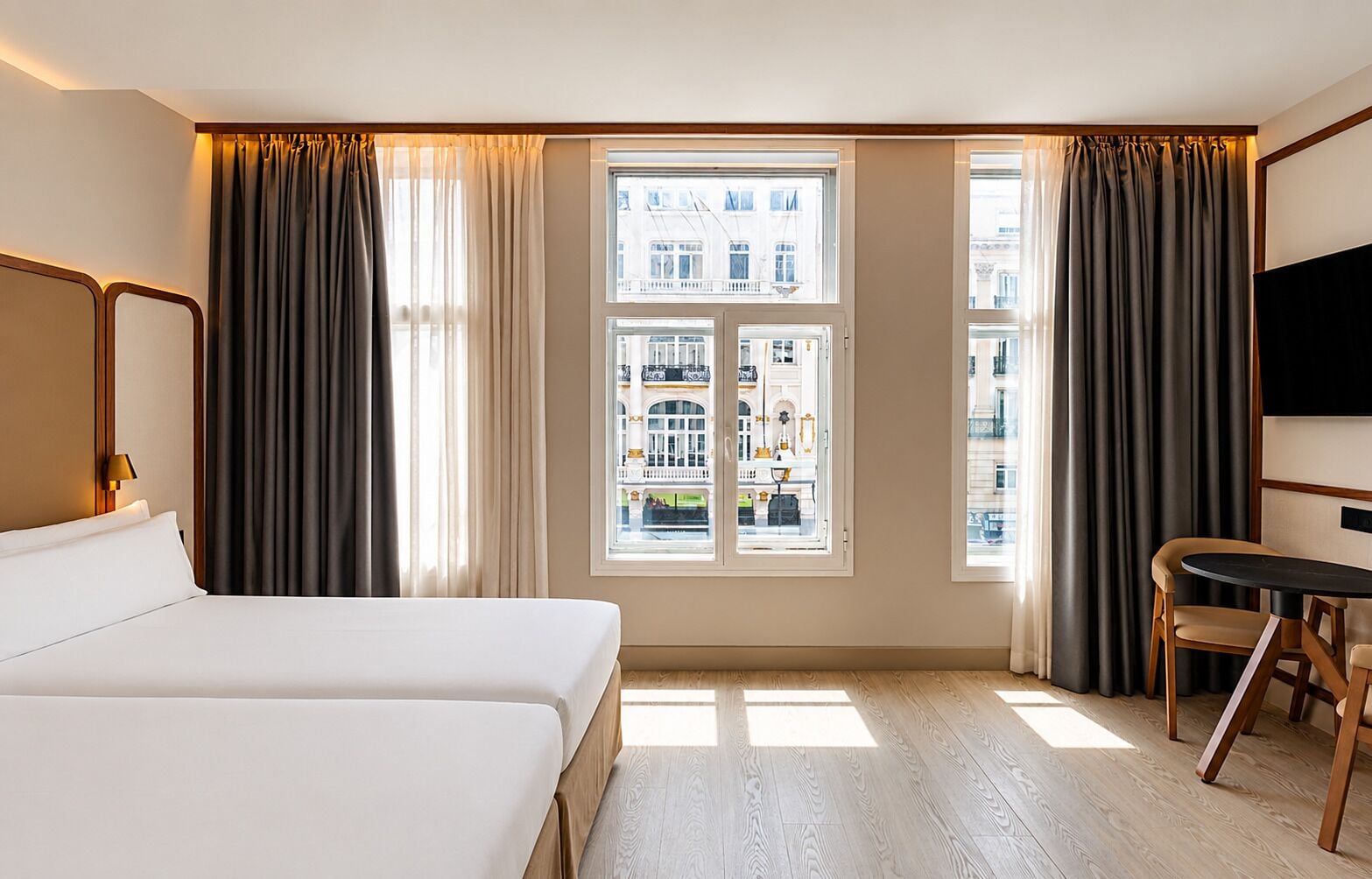 Een hotelkamer met een groot bed, een bureau en uitzicht op een stadslandschap door een raam.