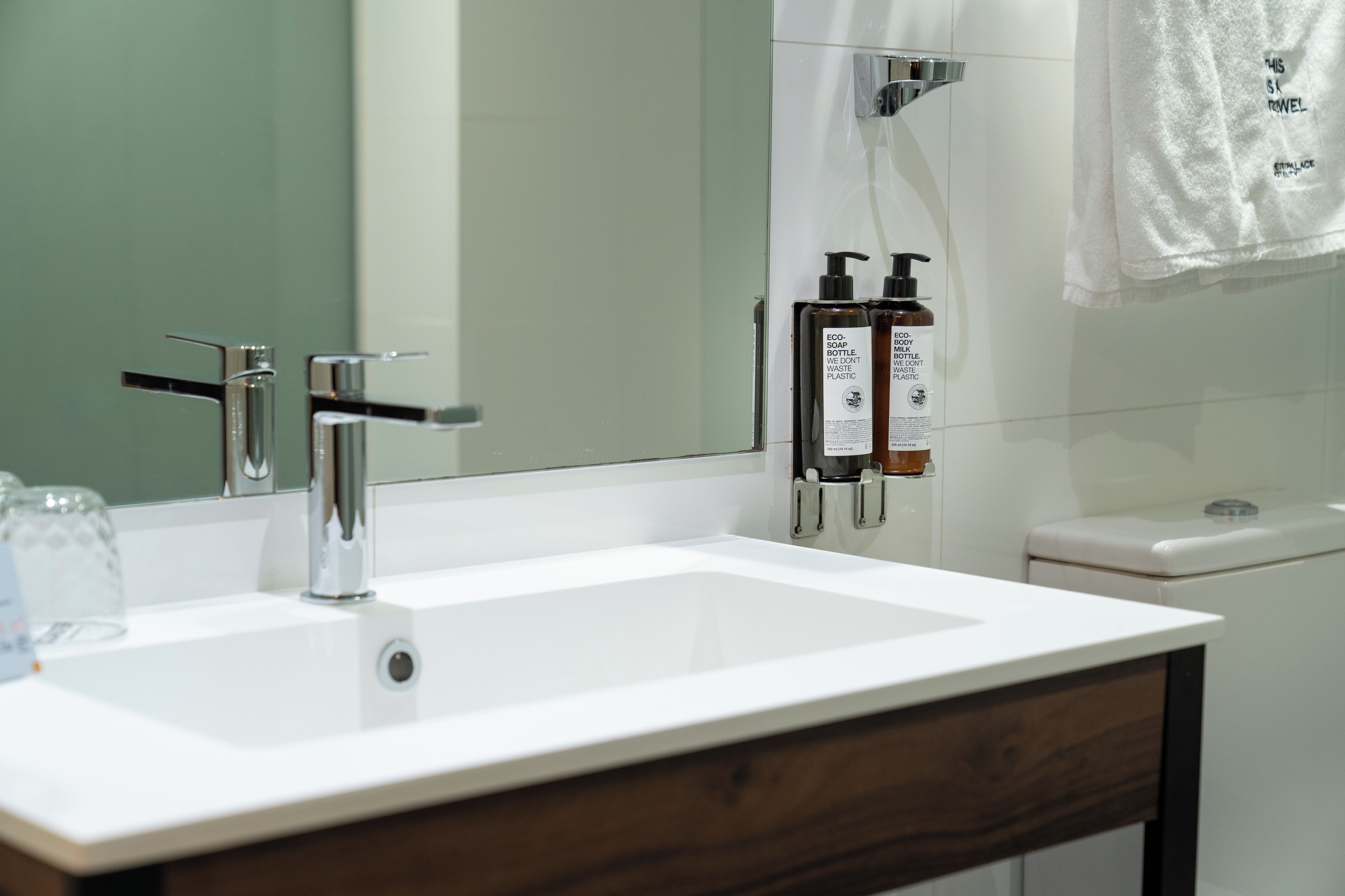 Un baño con lavamanos blanco, grifo cromado y dos botellas de jabón.