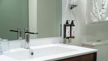 Un baño con lavamanos blanco, grifo cromado y dos botellas de jabón.