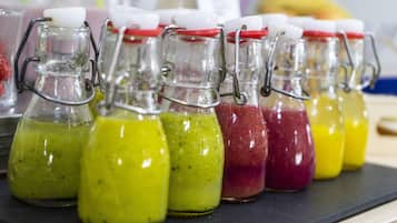 Una fila di bottiglie di vetro con chiusure metalliche, ognuna contenente un liquido di colore diverso, disposte su una superficie nera.