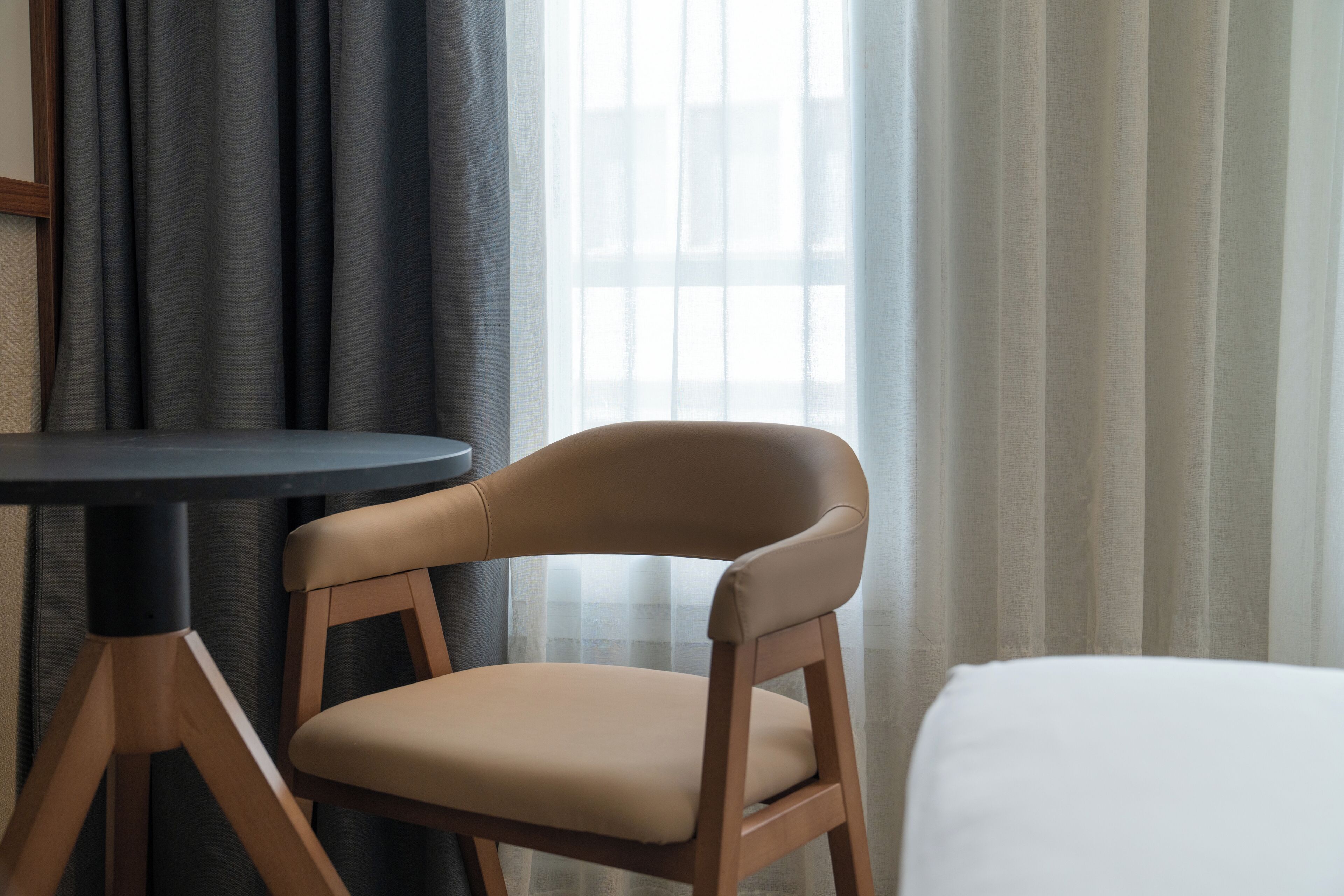 A hotel room with a single chair, a small table, and a bed.