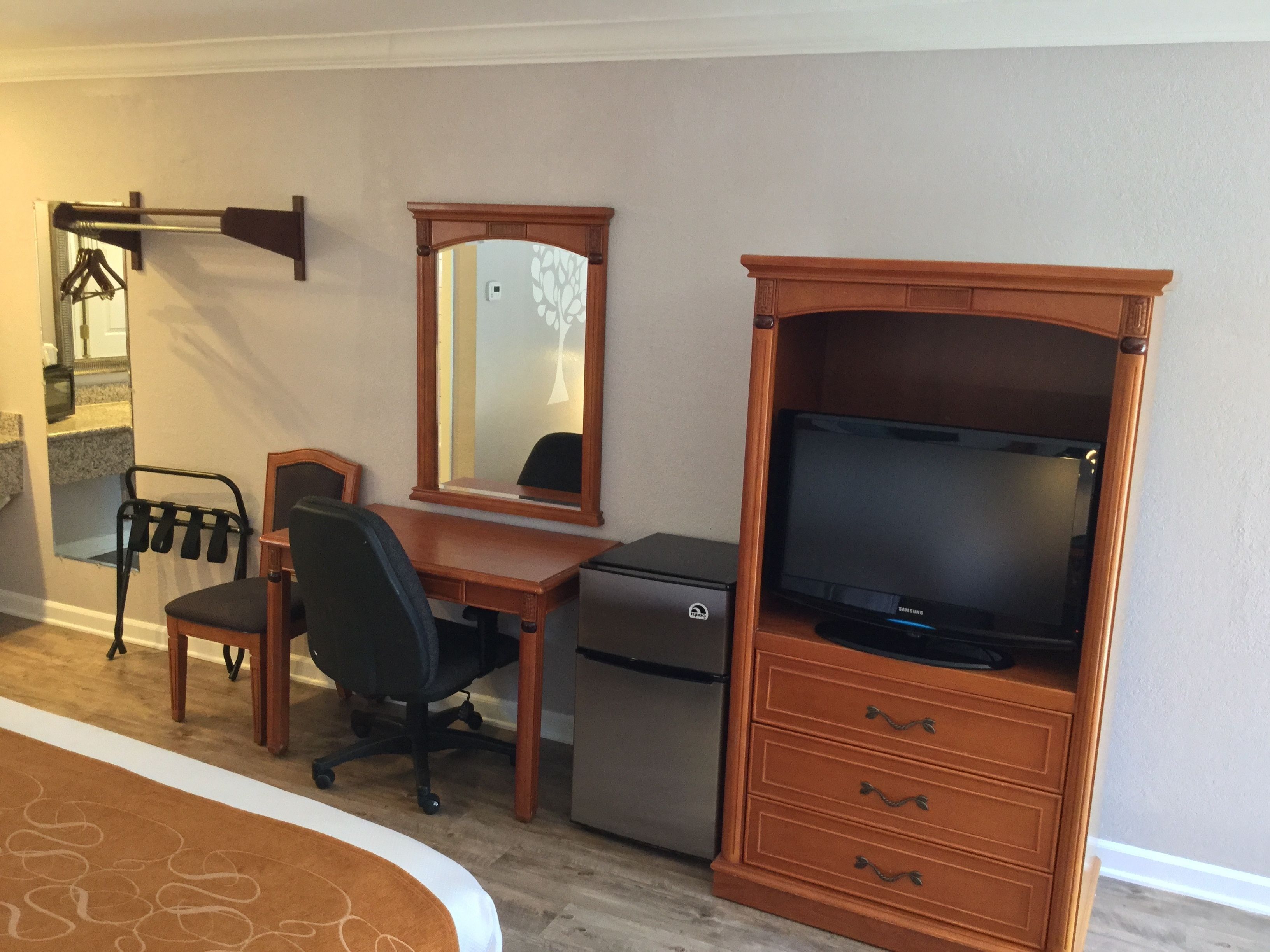 A bedroom with a bed, a desk with a computer, a chair, a dresser, and a mirror.