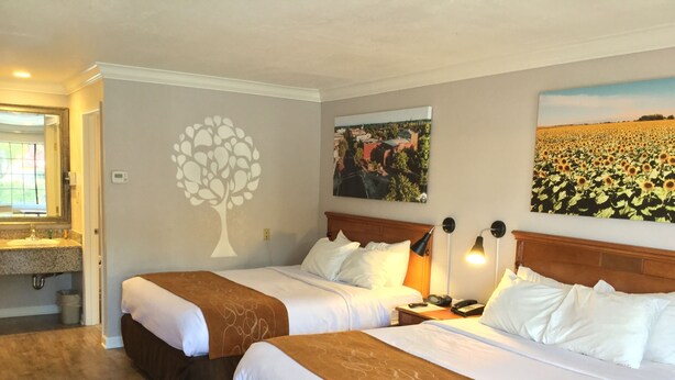 Une chambre d’hôtel avec deux lits, une grande fenêtre, un motif d’arbre décoratif sur le mur et un tableau représentant un champ de tournesols.