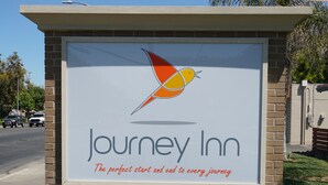 Une enseigne « Journey Inn » avec un logo représentant un oiseau et le slogan : « Le point de départ et d’arrivée idéal pour chaque voyage. »