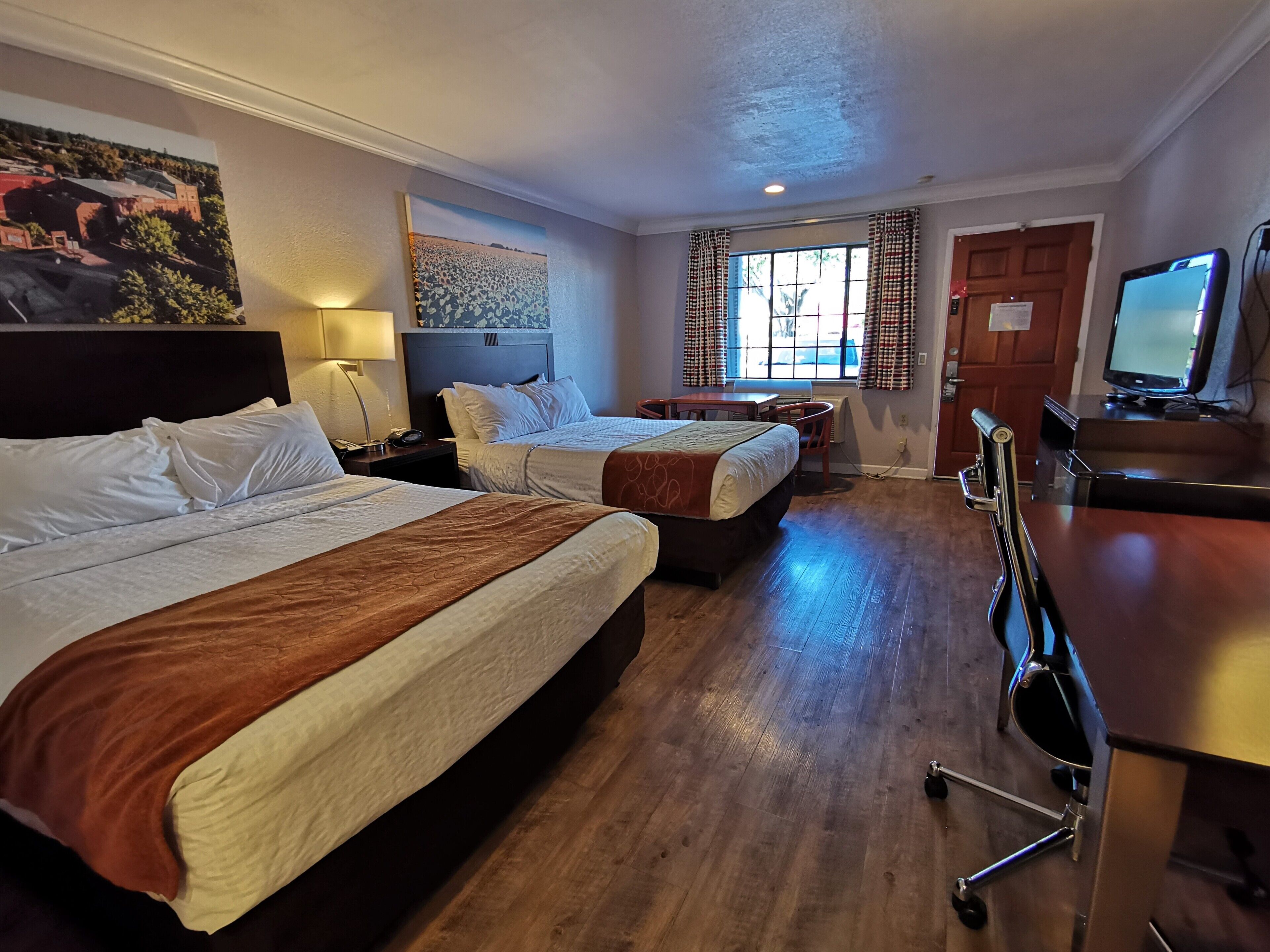 Una habitación de hotel con dos camas, un escritorio, una silla, un televisor y una ventana con cortinas.