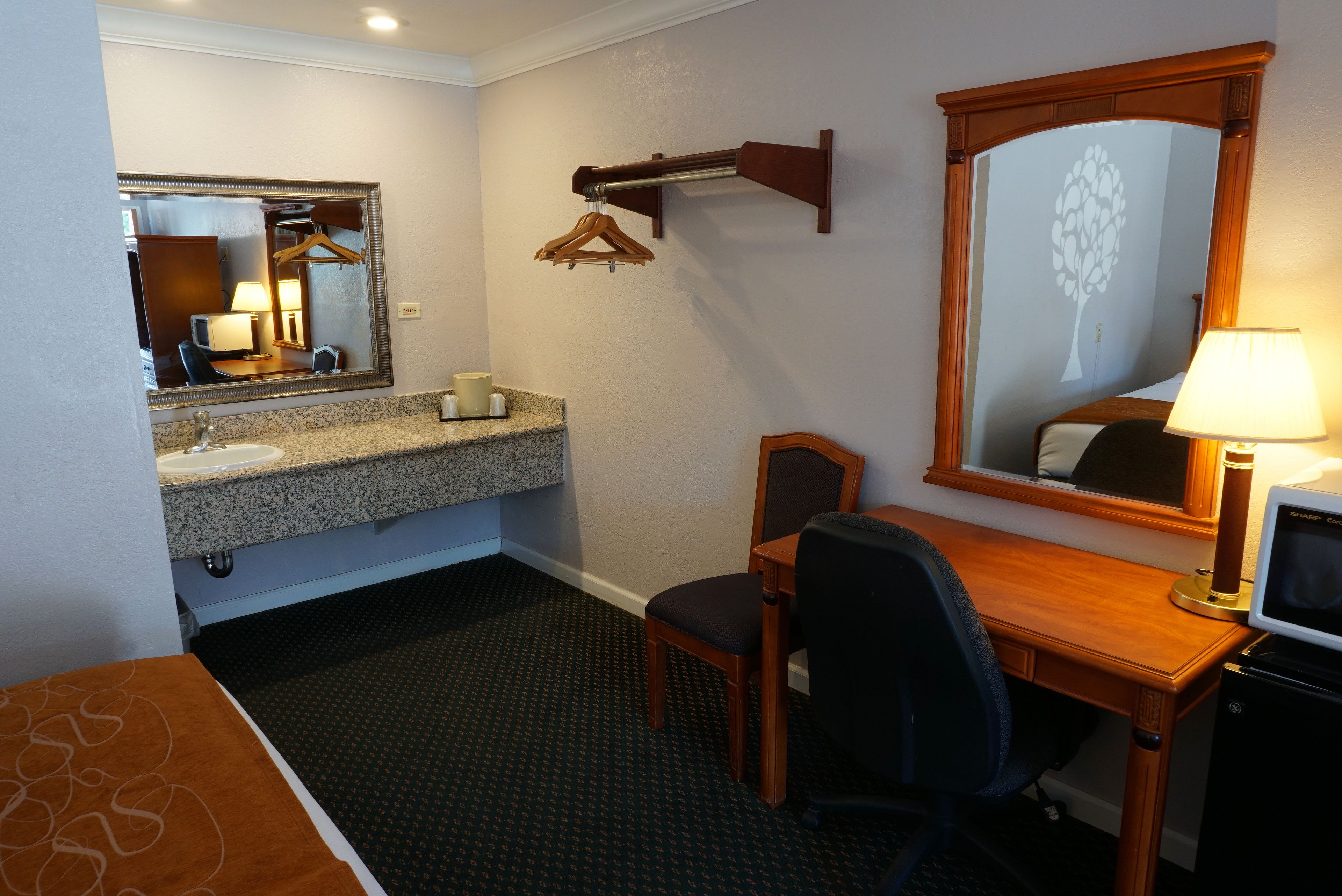 A hotel room with a granite countertop sink, a wooden desk, a chair, a television, and a large mirror.