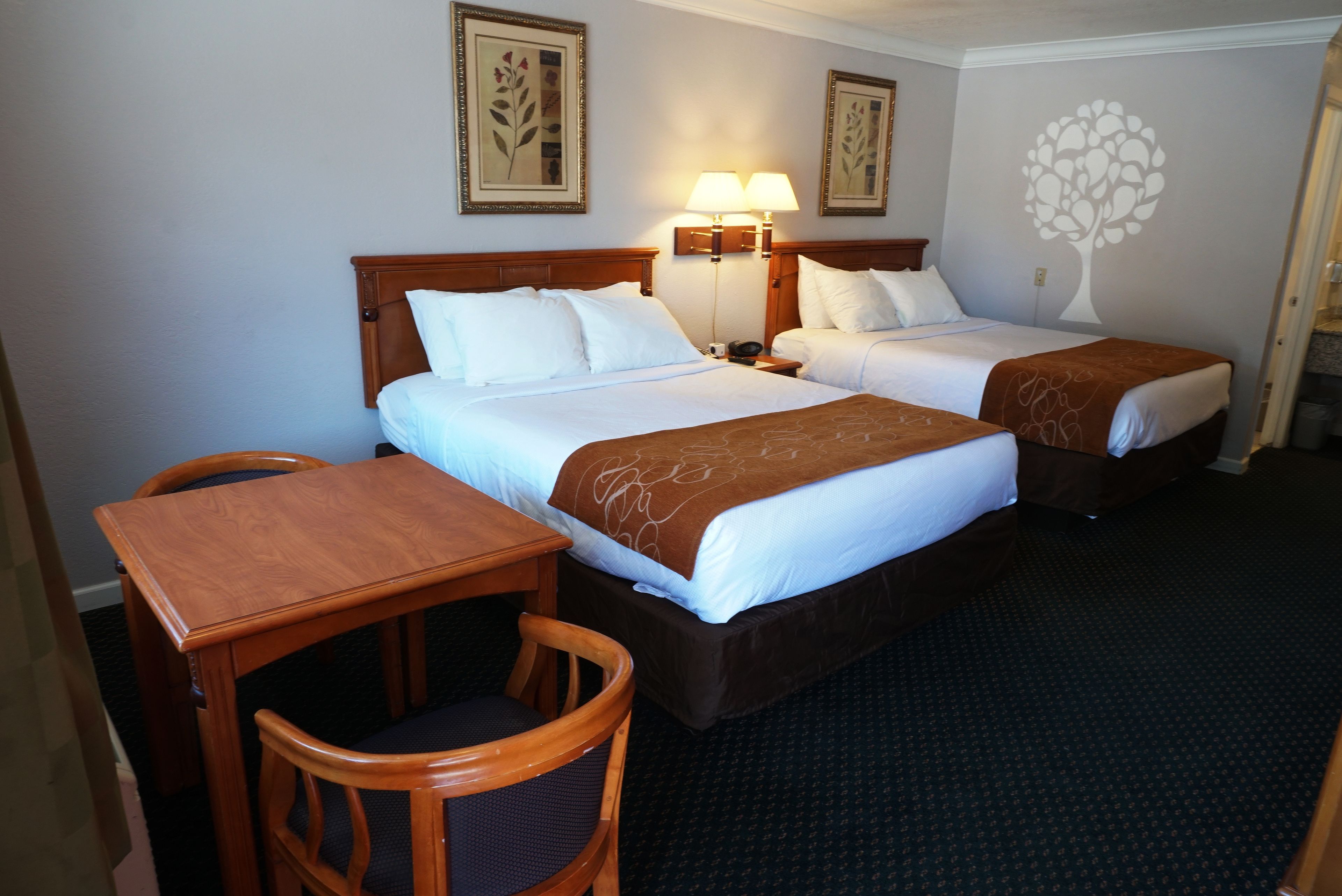 A hotel room with two beds, a wooden desk, and chairs.