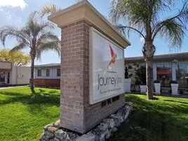 Un pilar de ladrillo con un letrero de Journey Inn, que presenta un logotipo de ave y la consigna 'El comienzo y final perfecto para cada viaje'.
