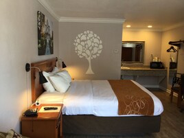 Habitación de hotel con cama, mesita de noche, lámpara y un adhesivo de árbol en la pared.