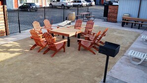 Une terrasse extérieure avec des tables et des chaises en bois, un barbecue noir et une glacière blanche.