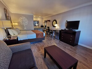 Ett hotellrum med en säng, ett skrivbord, en stol, en TV och en byrå.