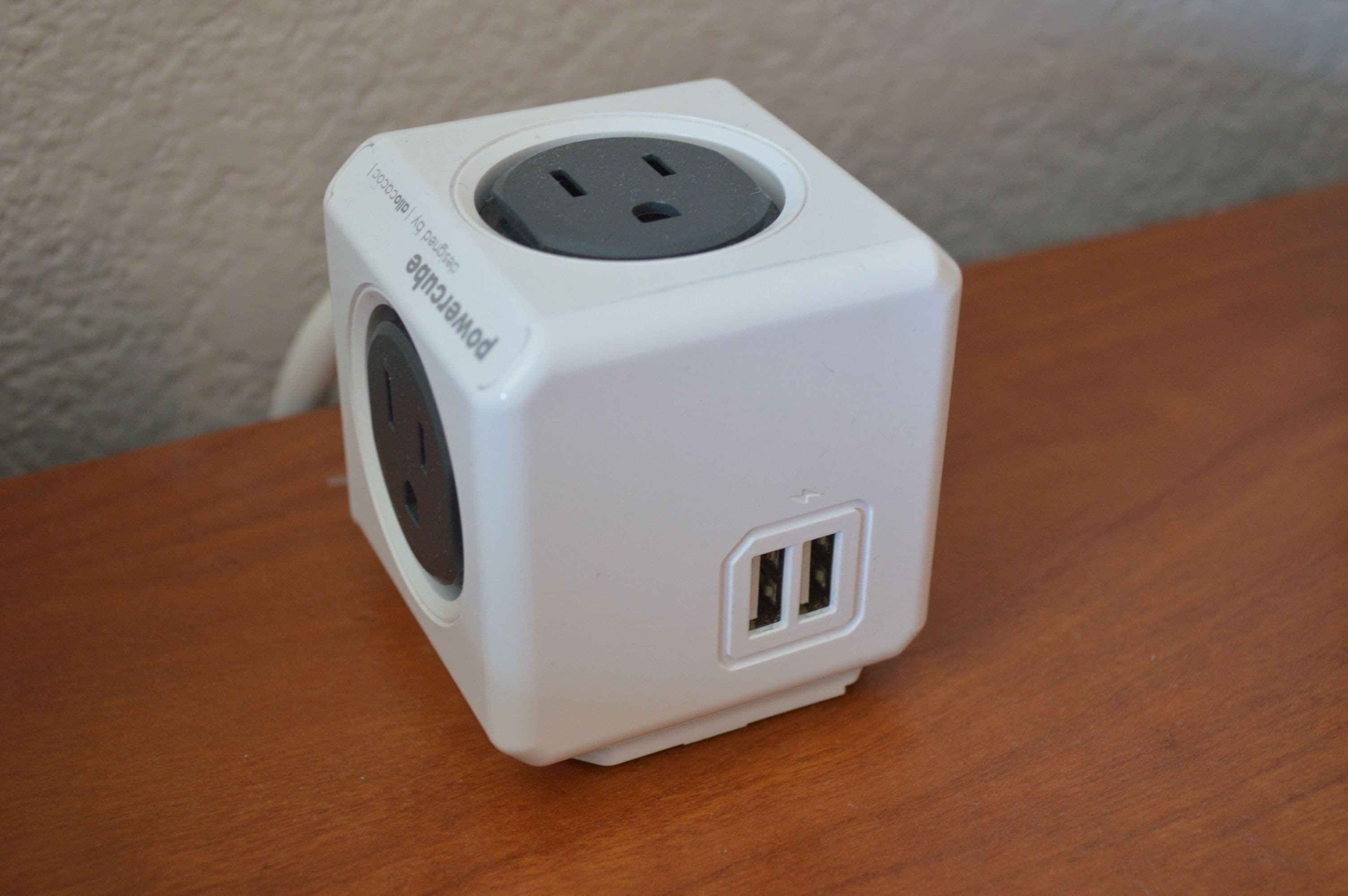 En vit grenuttag med två USB-portar och ett eluttag med tre stift, placerad på en träyta.