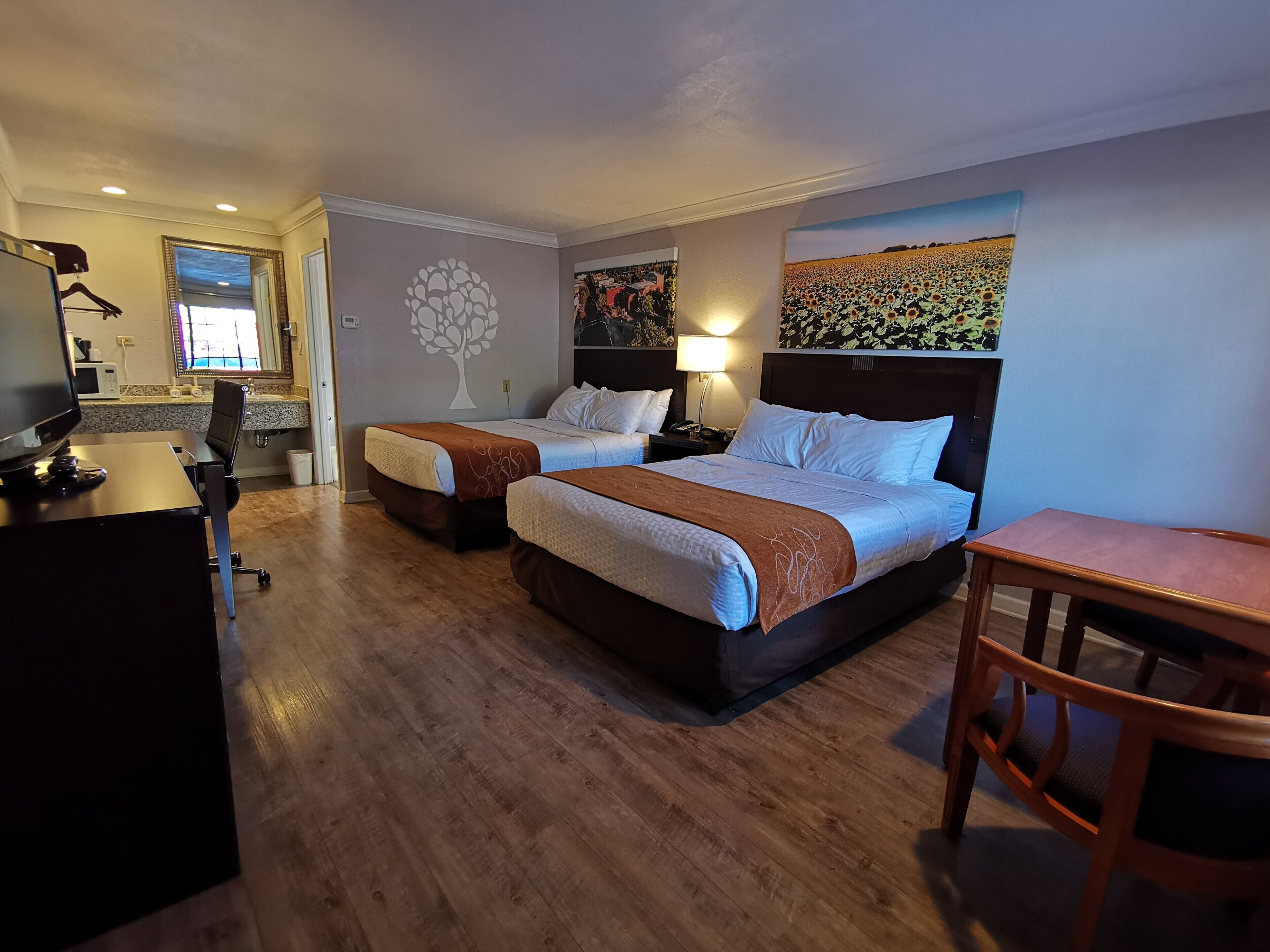 A hotel room with two beds, a desk with a computer, a chair, and a small table.