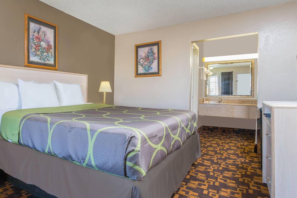 Une chambre d’hôtel avec un lit, un miroir dans la salle de bain et un sol à motifs.