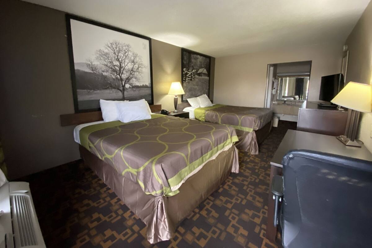 Une chambre d’hôtel avec deux lits, un bureau, une chaise, une lampe de bureau, un miroir et un téléviseur fixé au mur.
