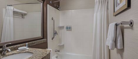 A bathroom with a granite countertop sink, a white toilet, a bathtub, and a shower curtain.