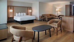 Una habitación de hotel moderna con una cama grande, dos sillones, una mesita, un escritorio y un armario.