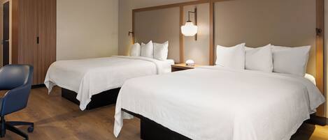 A hotel room with two beds, a desk, and a chair.