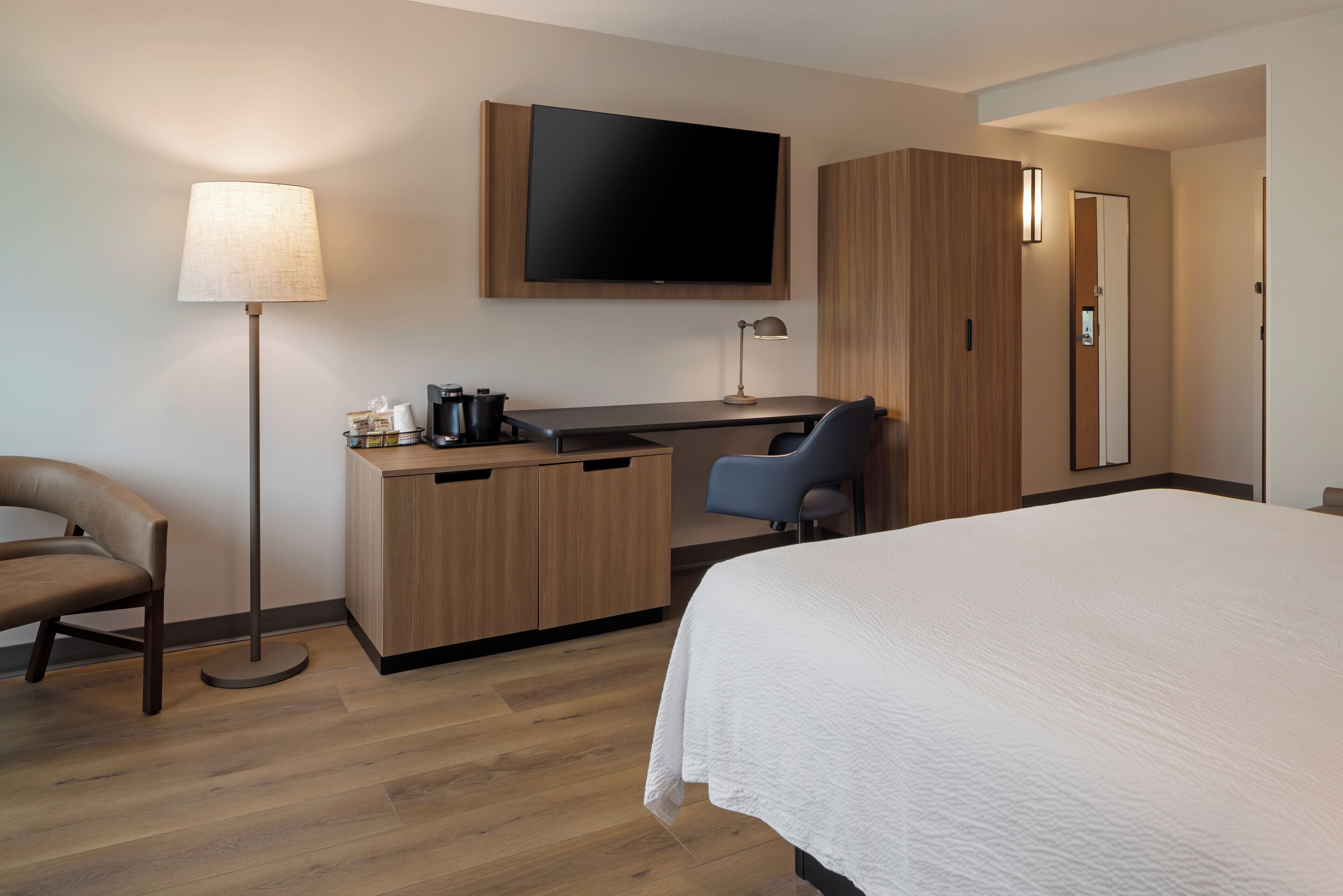 A hotel room with a bed, desk, chair, and a television mounted on the wall.