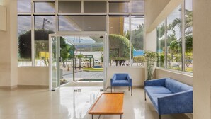 A modern lobby with a glass door leading outside, a blue sofa, a wooden table, and a blue armchair. - City Express by Marriott Tuxtla Gutierrez (Tuxtla Gutierrez)