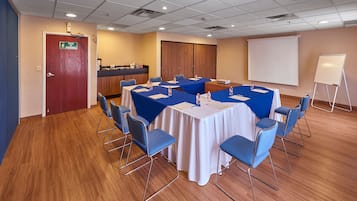 A conference room with a round table, blue chairs, a whiteboard, and a projection screen.